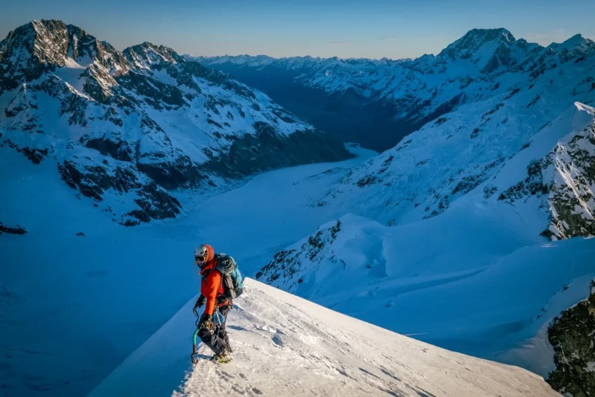 A mountaineer on a sunlit snow ridge above a glacier and alpine valley