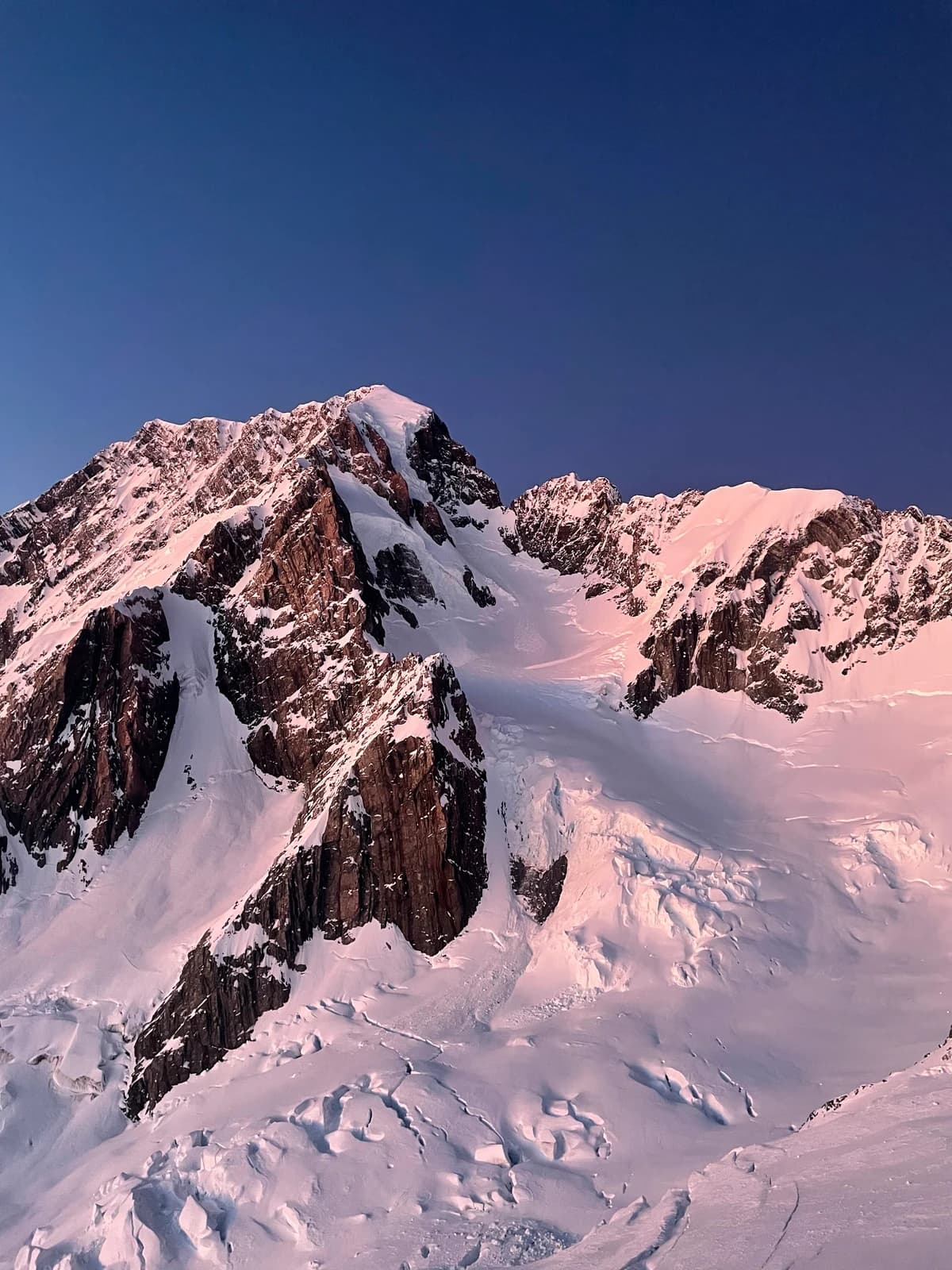First pink light on a snow-covered face in the Southern Alps